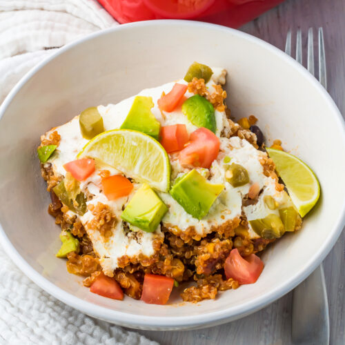 Quinoa Enchilada Casserole in a white bowl with a large red casserole dish in the background.