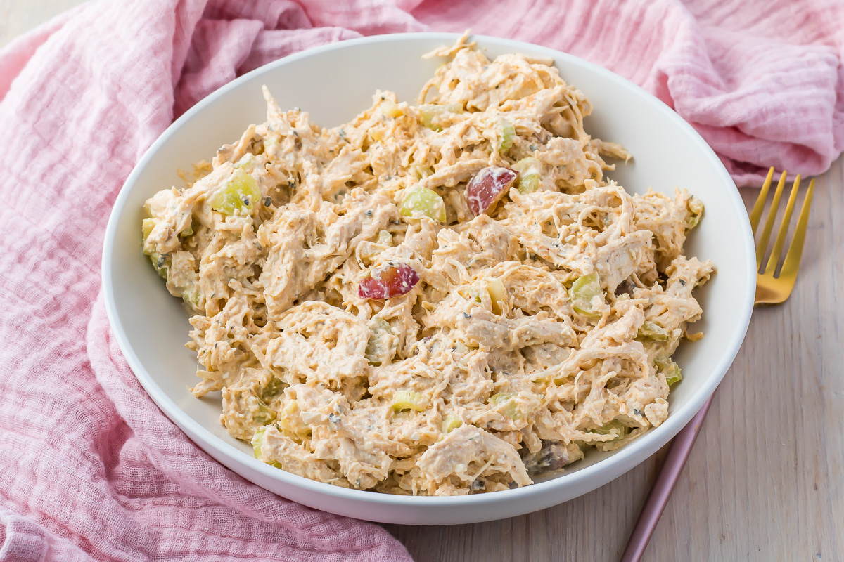Side photo of a bowl of high protein chicken salad, on a table with a pink cloth and fork.