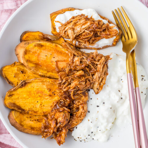 Overhead photo of a bbq chicken cottage cheese bowl in a white pasta bowl with a golden pink fork and knife, surrounded by a pink cloth.