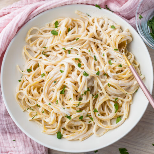 Cottage cheese alfredo in a white bowl with a pink and gold fork, and a pink cloth.
