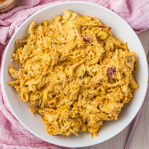 Overhead photo of a bowl of high protein curry chicken salad, on a table with a pink cloth and fork.