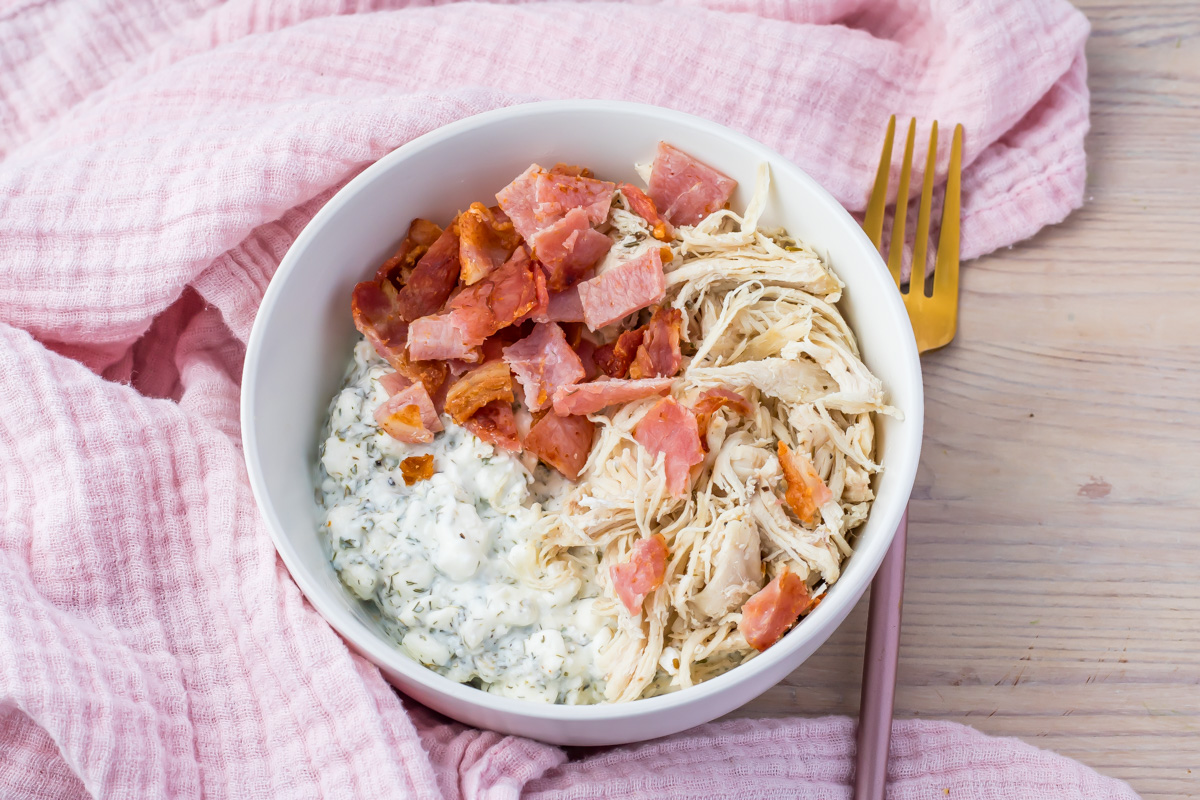 Overhead photo of a chicken bacon ranch cottage cheese bowl next to a pink cloth and pink and gold fork.