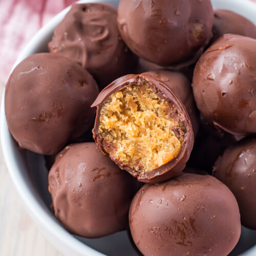 A bowl of chocolate-covered protein balls, with one showcasing a bite that reveals the creamy peanut butter filling inside.