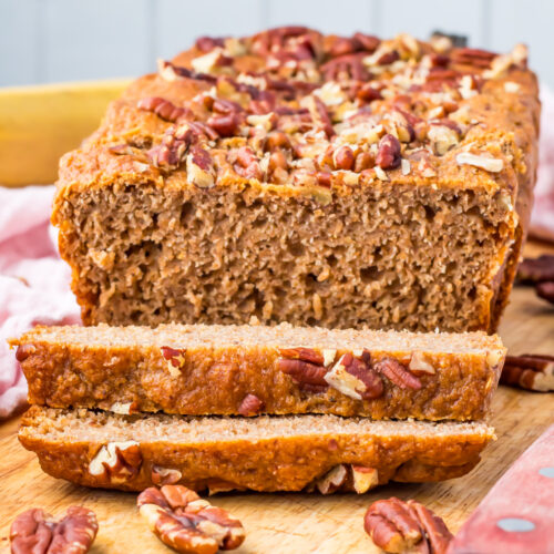 A loaf of cottage cheese banana bread topped with pecans, with two slices cut in front, rests invitingly on a wooden board.