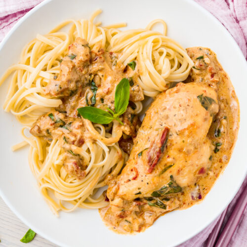 Indulge in a plate of creamy Tuscan Chicken, an exquisite Italian dish with sun-dried tomatoes and spinach, served alongside linguine pasta and garnished with fresh basil.