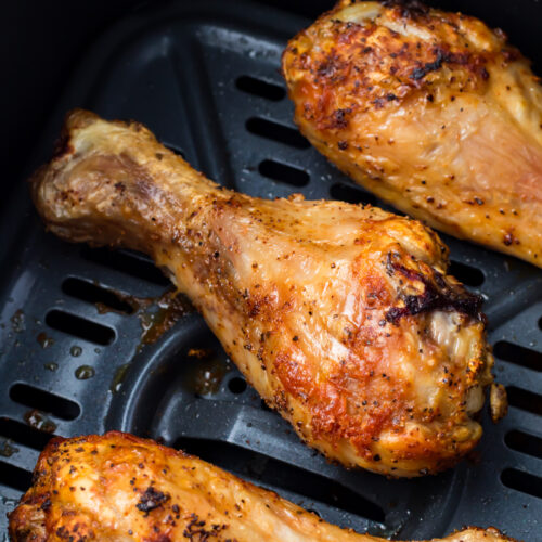 Roasted Air fryer chicken legs with a crispy, golden skin in a black air fryer basket.