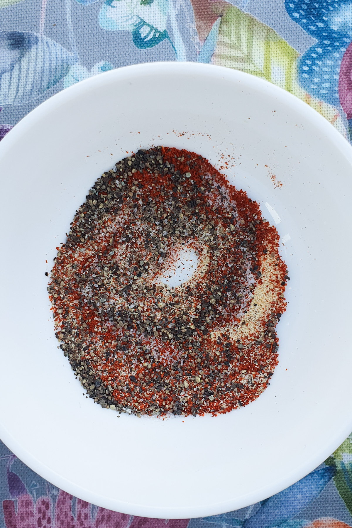 A white bowl contains a vibrant mix of black, red, and yellow spices.