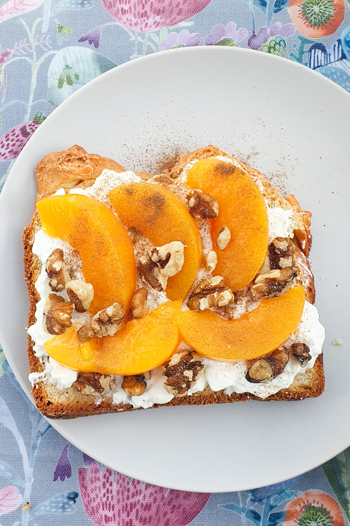 Air fryer toast topped with cottage cheese, peach slices, walnuts, and a sprinkle of cinnamon on a white plate.