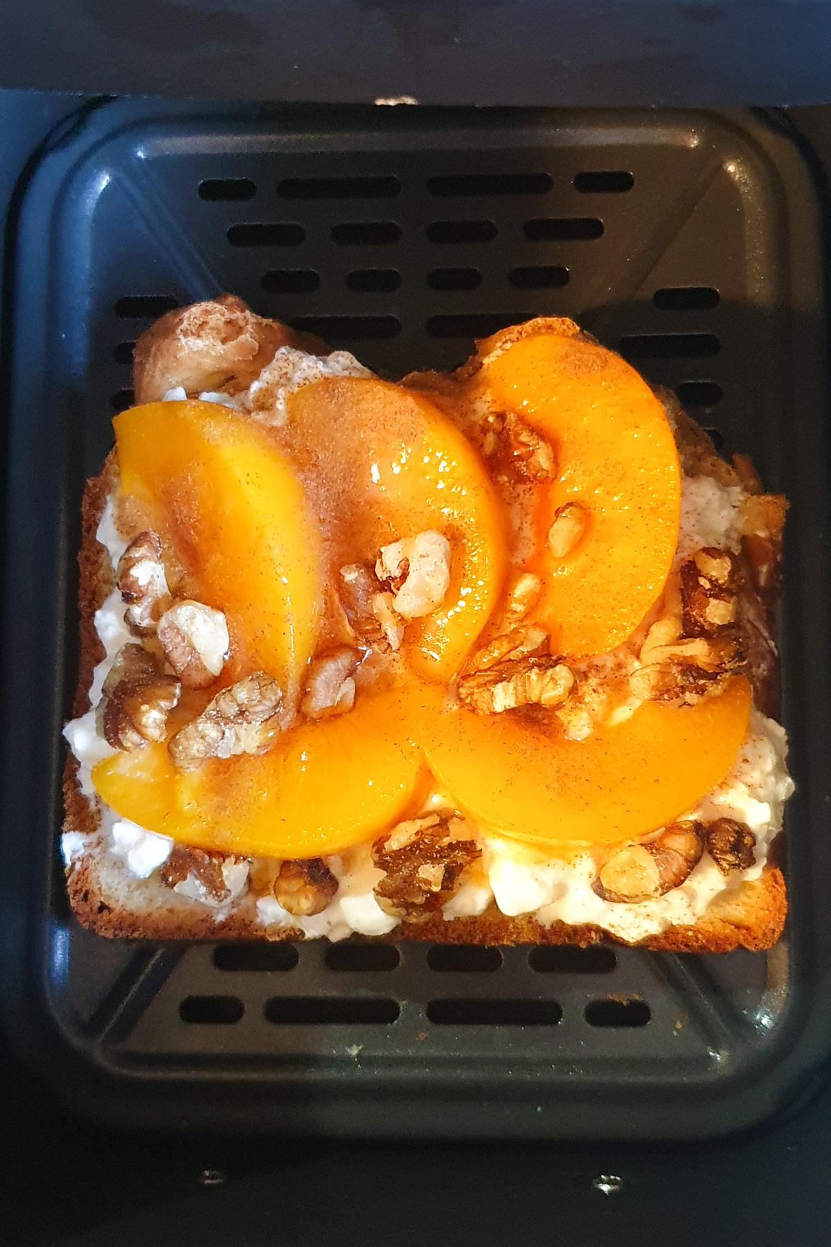 Toast topped with creamy cottage cheese, sliced peaches, and crunchy walnuts sits perfectly in the air fryer basket.