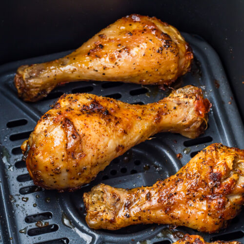 Three cooked hot honey chicken drumsticks in an air fryer basket.