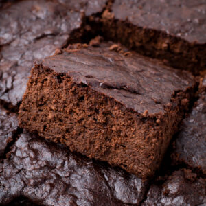 Close-up of a batch of thick, fudgy cottage cheese brownies. One piece is slightly raised above the others.