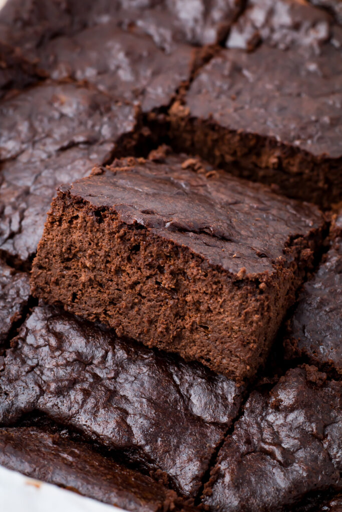 A batch of chocolate cottage cheese brownies, with one piece slightly elevated, displaying a rich, dense texture.