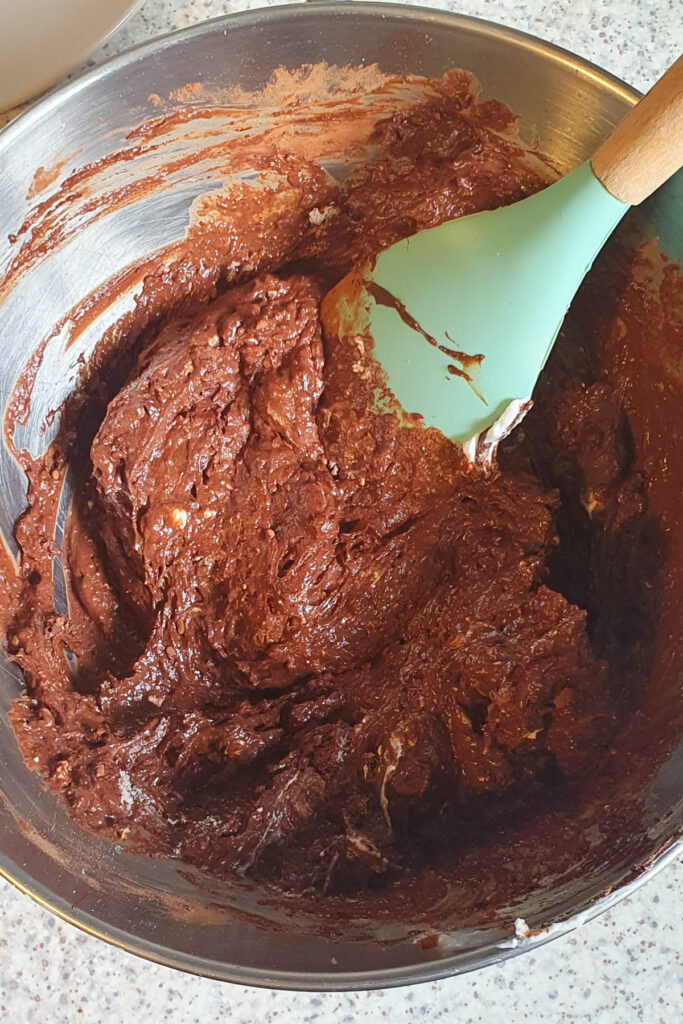 A bowl of chocolate brownie batter is being mixed with a green spatula.