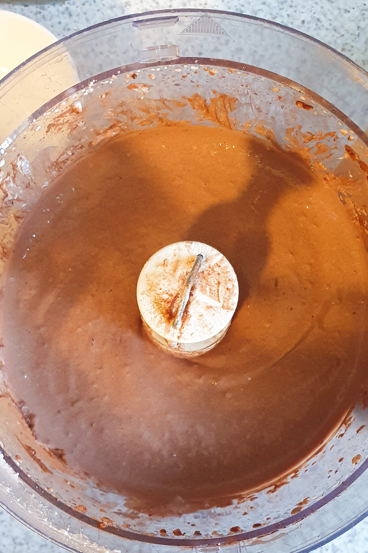Cottage cheese mousse in a food processor bowl with a central blade, all set on a speckled countertop.