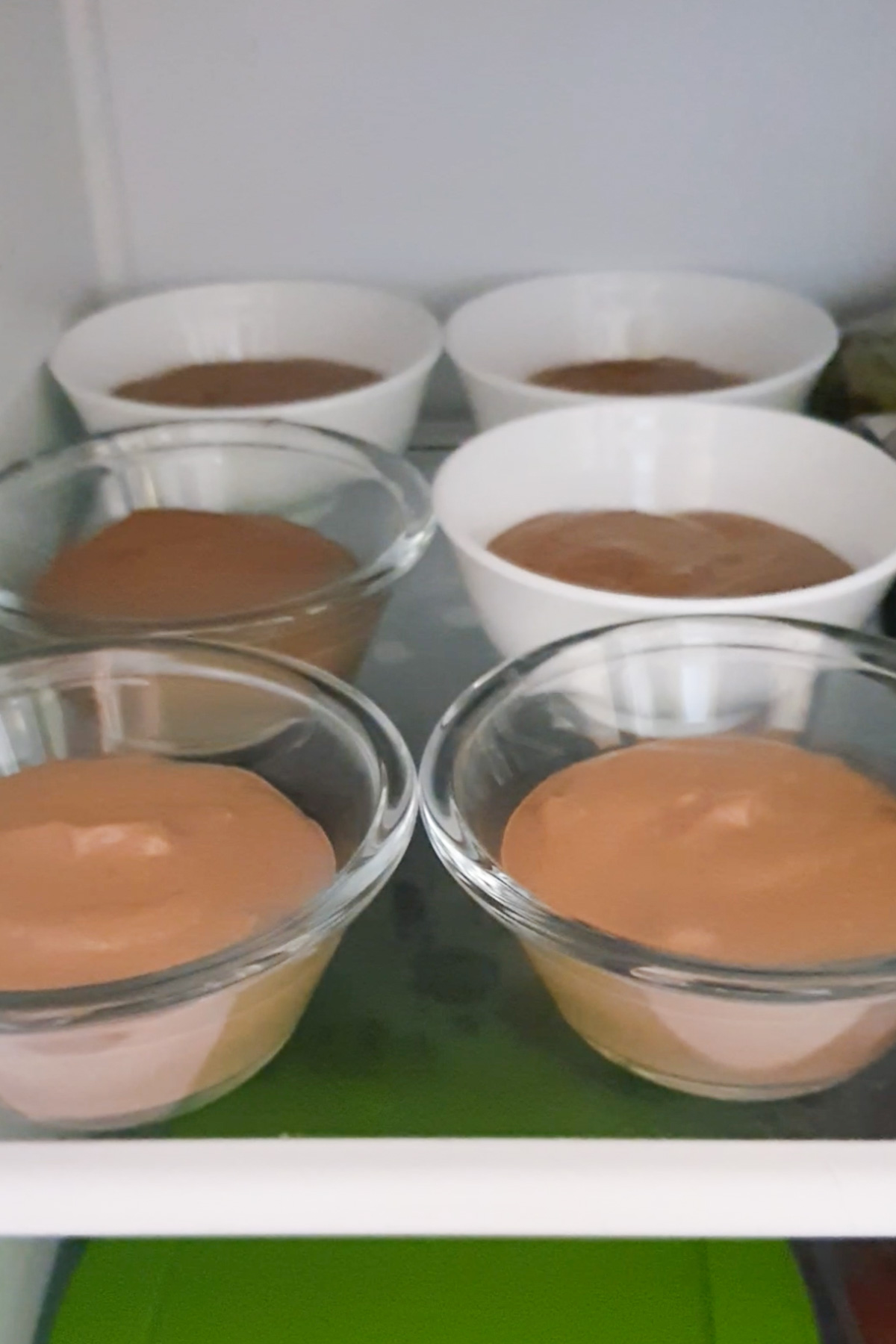 Several bowls of chocolate mousse elegantly arranged in a fridge.