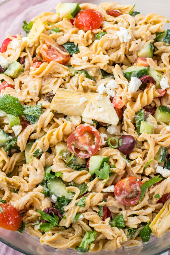 A high-protein pasta salad featuring chickpea pasta, cherry tomatoes, cucumbers, olives, feta cheese, and a sprinkle of fresh herbs.