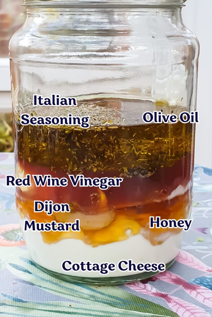 Layered ingredients in a jar: cottage cheese, honey, Dijon mustard, red wine vinegar, olive oil, and Italian seasoning complement your salad.