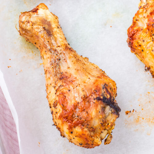 Oven baked chicken drumstick with a seasoned, crispy brown exterior rests on white parchment paper.