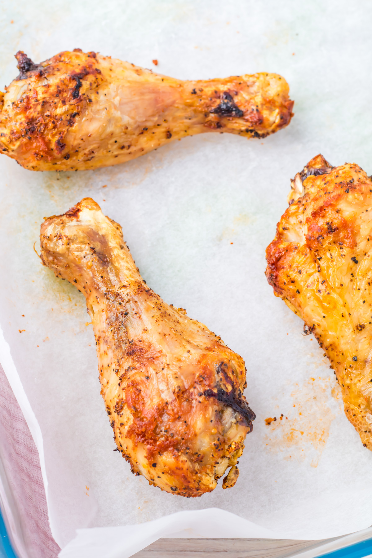Three seasoned and oven-baked drumsticks rest on parchment paper.