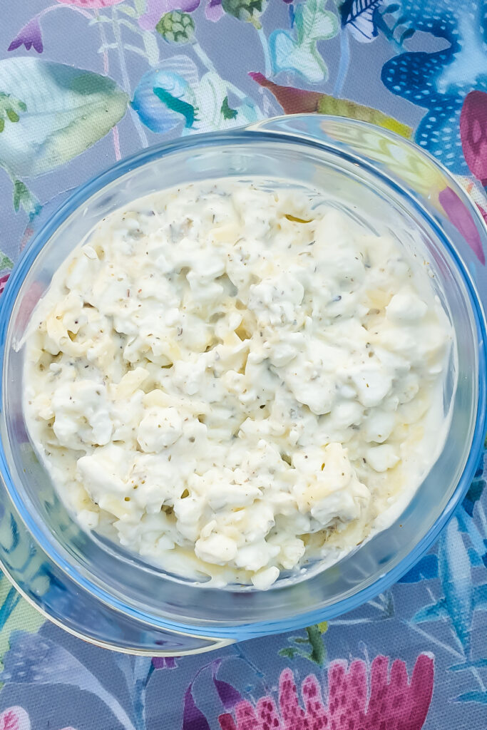 A clear glass bowl brimming with a cottage cheese base for a pizza bowl sits on a colorful, patterned tablecloth.