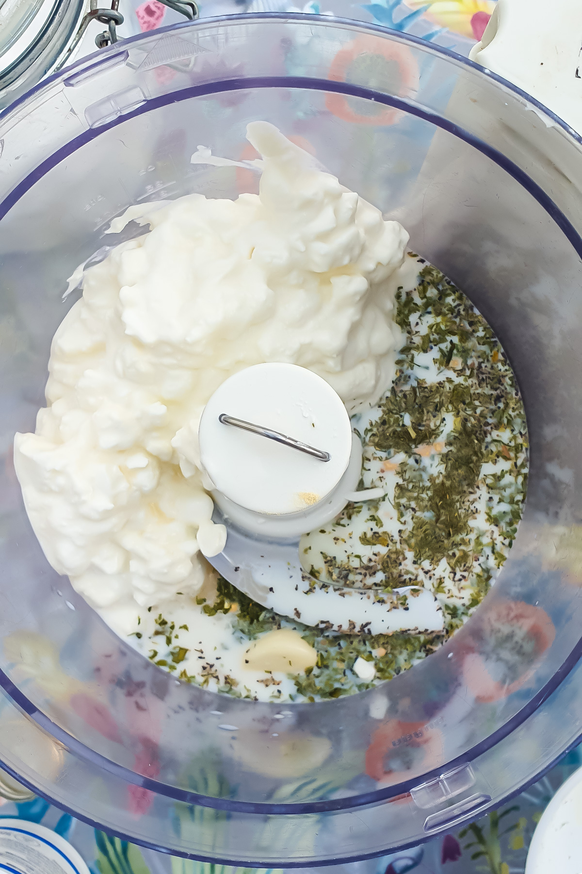 Food processor bowl with cottage cheese, herbs, garlic, and milk.