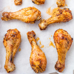 Seven seasoned and cooked hot honey chicken drumsticks rest on parchment paper.