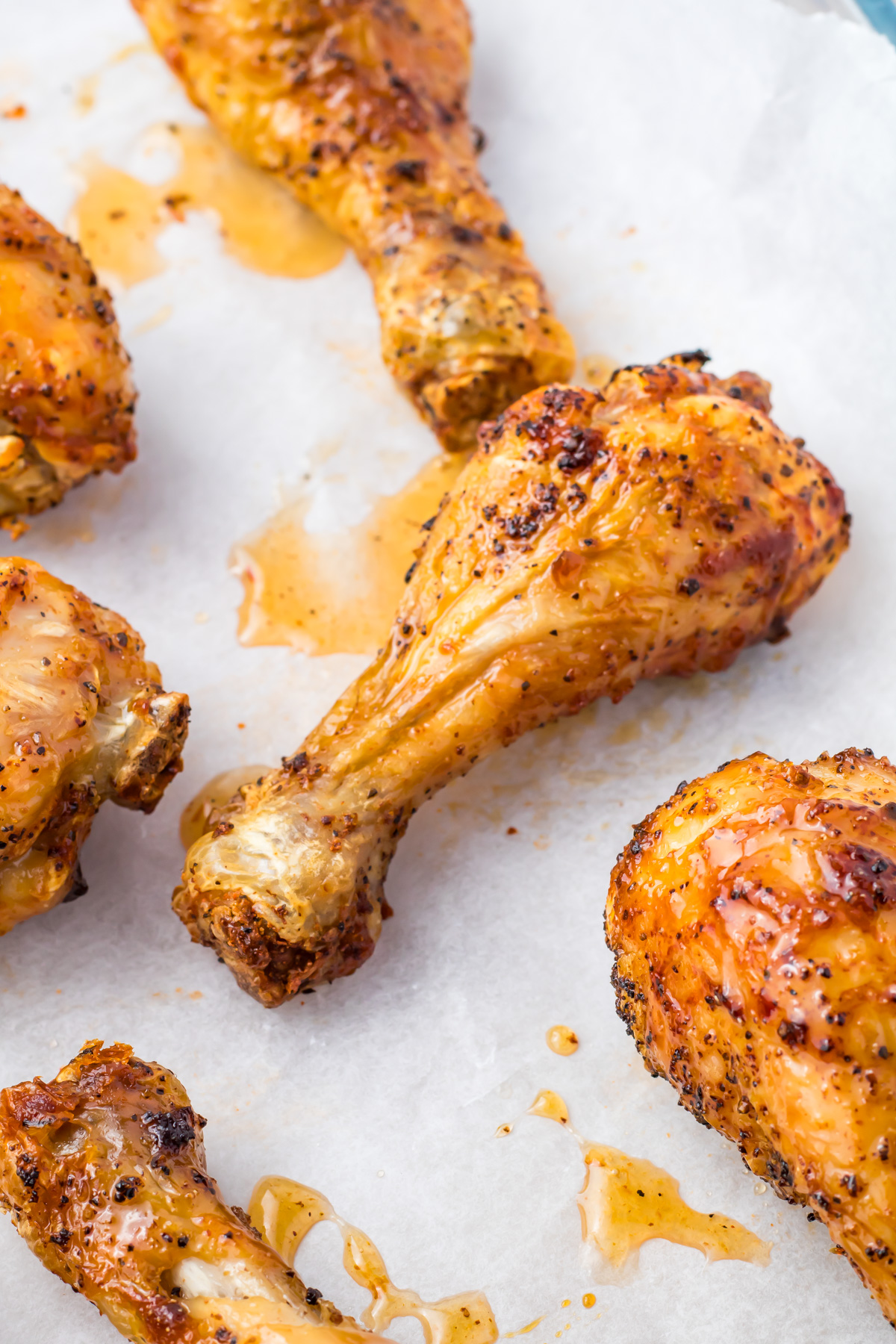 Several seasoned and cooked hot honey chicken drumsticks rest enticingly on a white parchment sheet.
