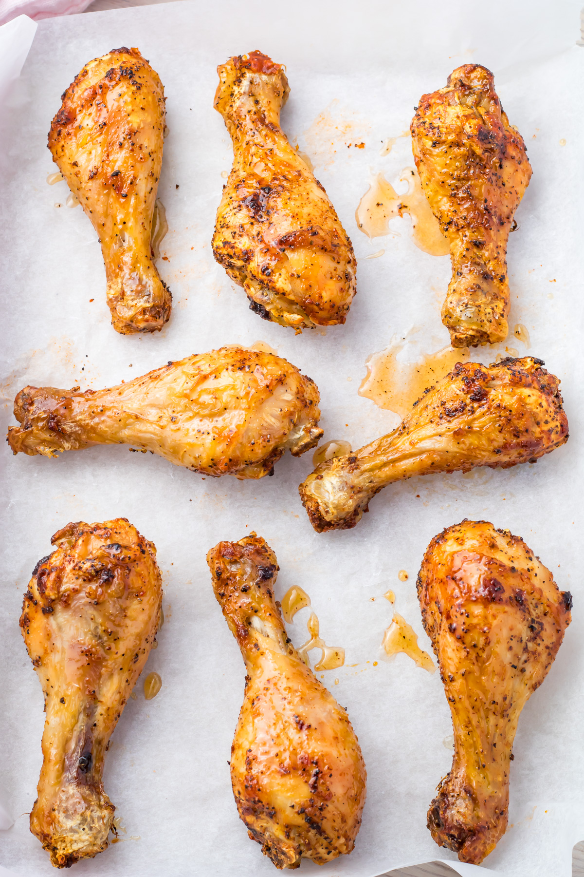 Eight seasoned hot honey chicken drumsticks, roasted to perfection, rest enticingly on parchment paper.