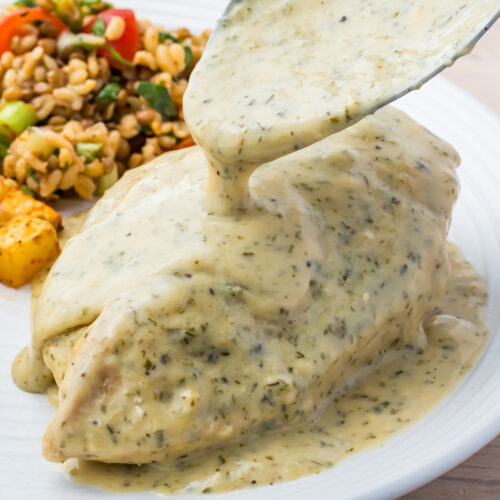 A rich sauce is poured over a perfectly cooked ranch chicken breast, nestled beside a vibrant array of mixed vegetables and grains.