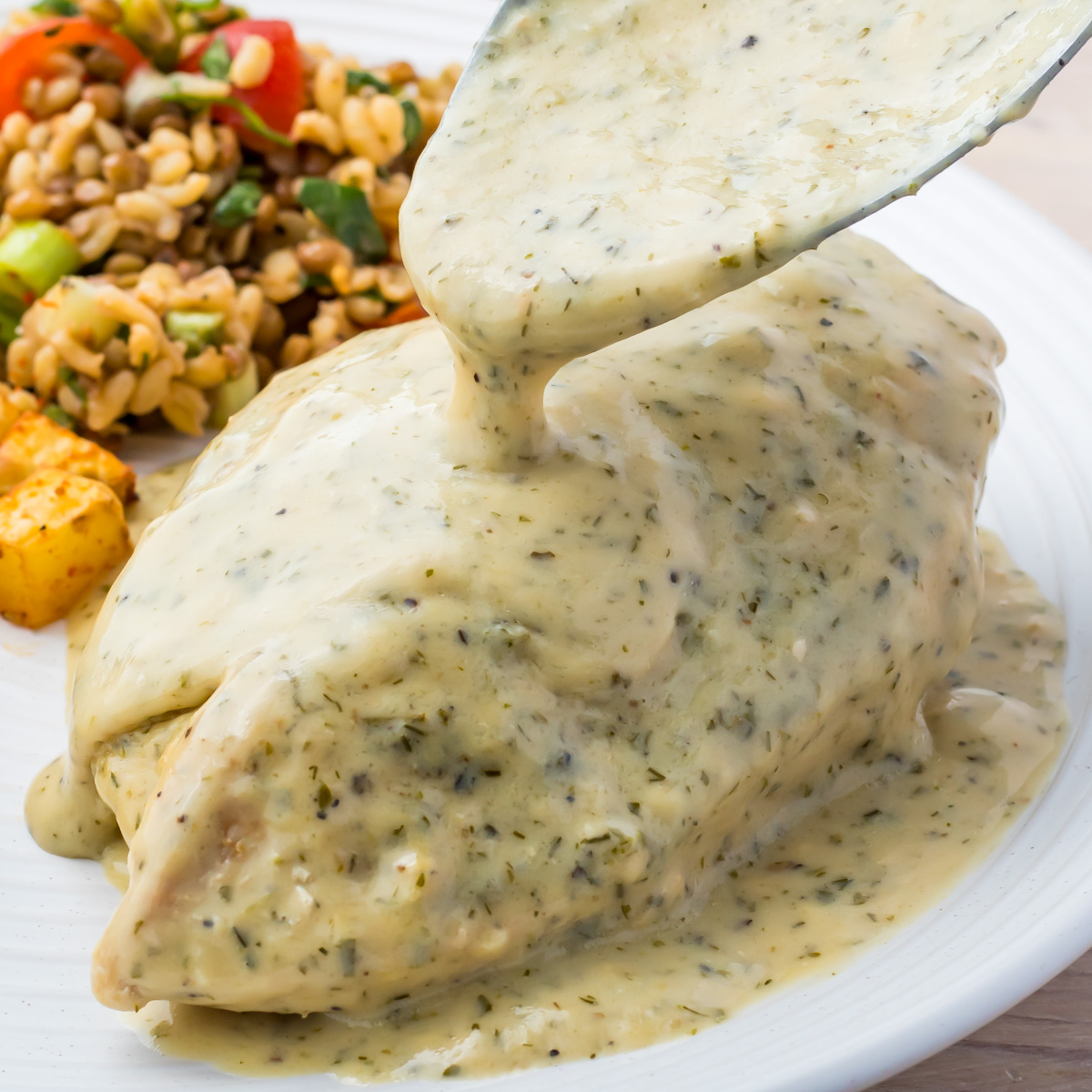 A rich sauce is poured over a perfectly cooked ranch chicken breast, nestled beside a vibrant array of mixed vegetables and grains.