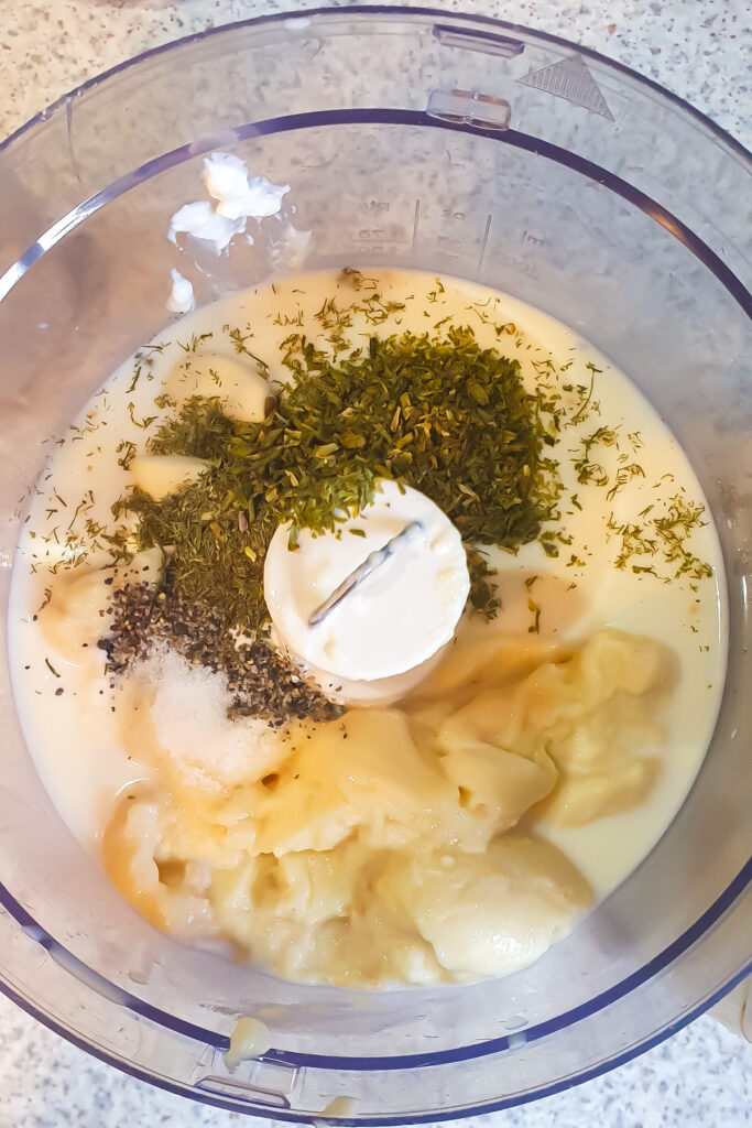 Ingredients for a flavorful ranch sauce in a food processor: condensed chicken soup, cottage cheese, milk, herbs, and spices.