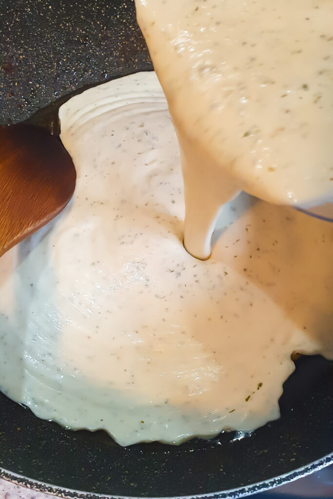 Ranch sauce is being poured into a frying pan, with a wooden spoon partially visible on the side.