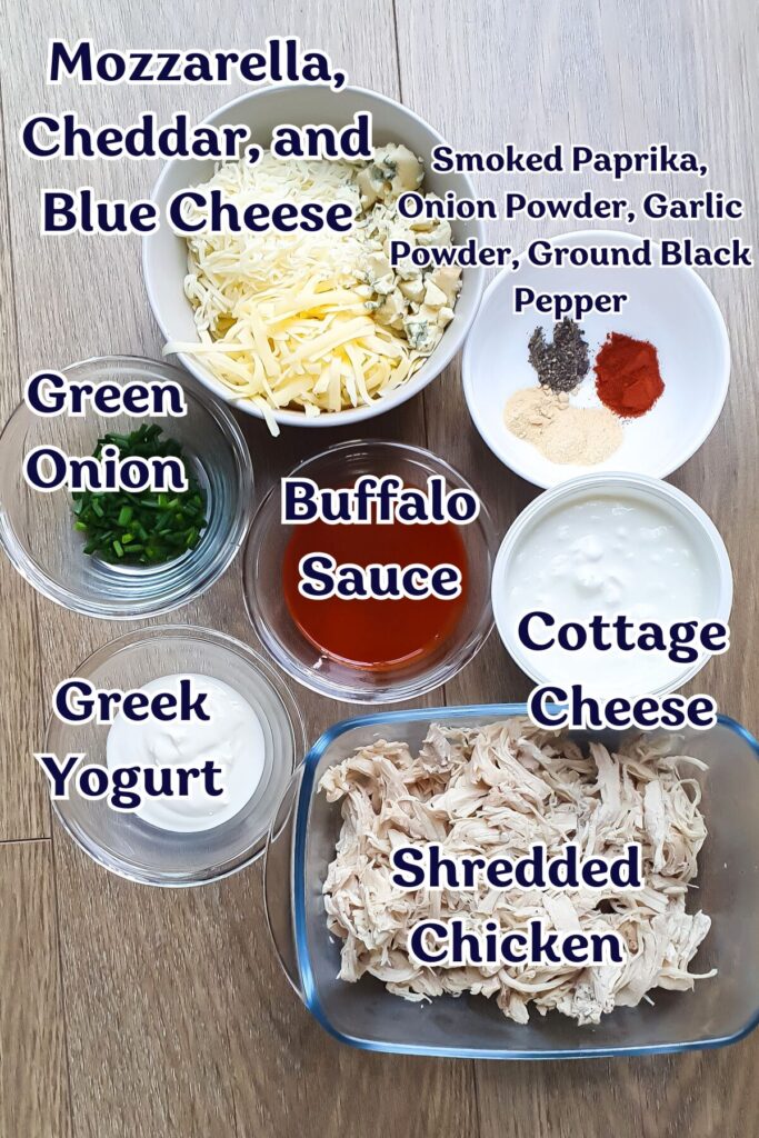 Ingredients for Buffalo Chicken Dip with cottage cheese, including shredded chicken, cottage cheese, Greek yogurt, buffalo sauce, green onion, mixed cheeses, and seasonings, are displayed in bowls.