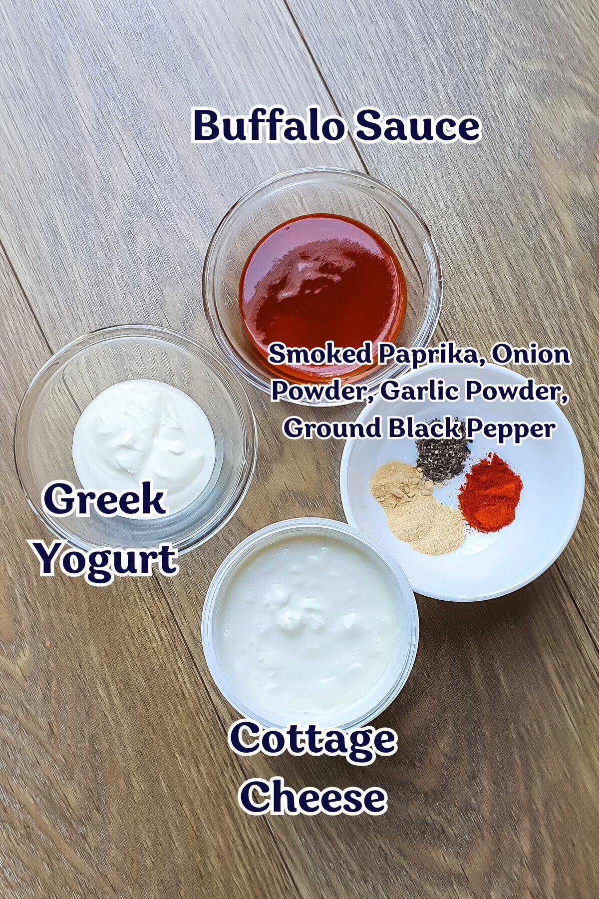 Four bowls on a wooden surface contain buffalo sauce, Greek yogurt, cottage cheese, and a mix of spices—perfect for creating a creamy cottage cheese dip or flavorful buffalo dip.