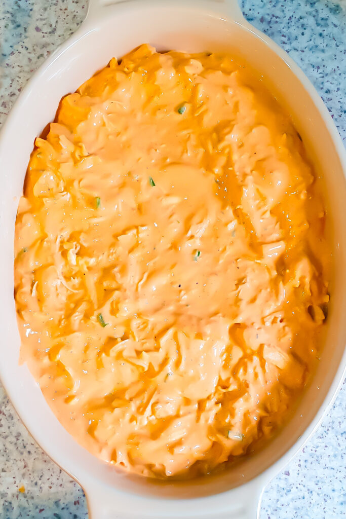 A white oval baking dish filled with an orange-colored creamy Buffalo Chicken Dip with cottage cheese, on a speckled countertop.