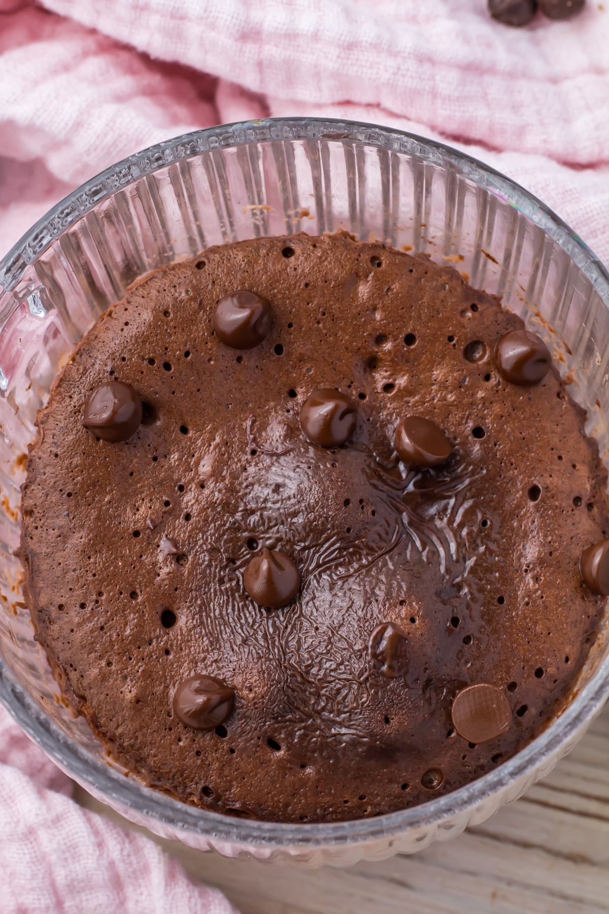 A close up of chocolate protein mug cake in a clear glass mug surrounded by a pink cloth.