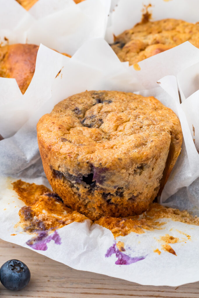 A close-up of a baked cottage cheese blueberry muffin on white parchment paper, with visible blueberries.