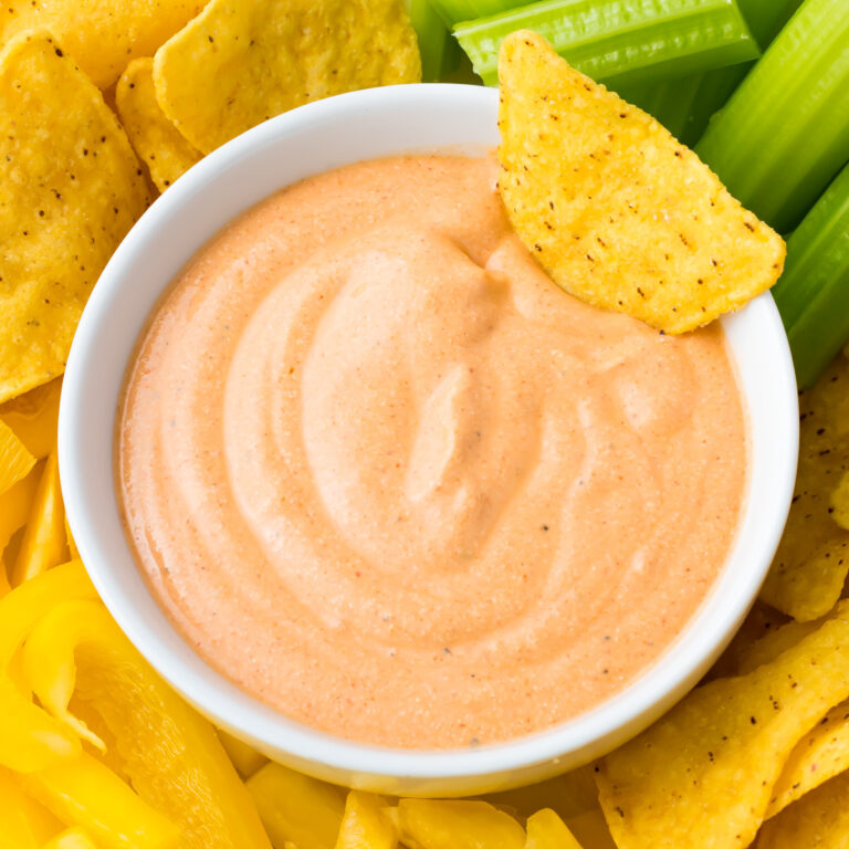 A bowl of creamy Cottage Cheese Buffalo Dip sits at the center, surrounded by yellow tortilla chips, celery sticks, and yellow bell pepper slices.