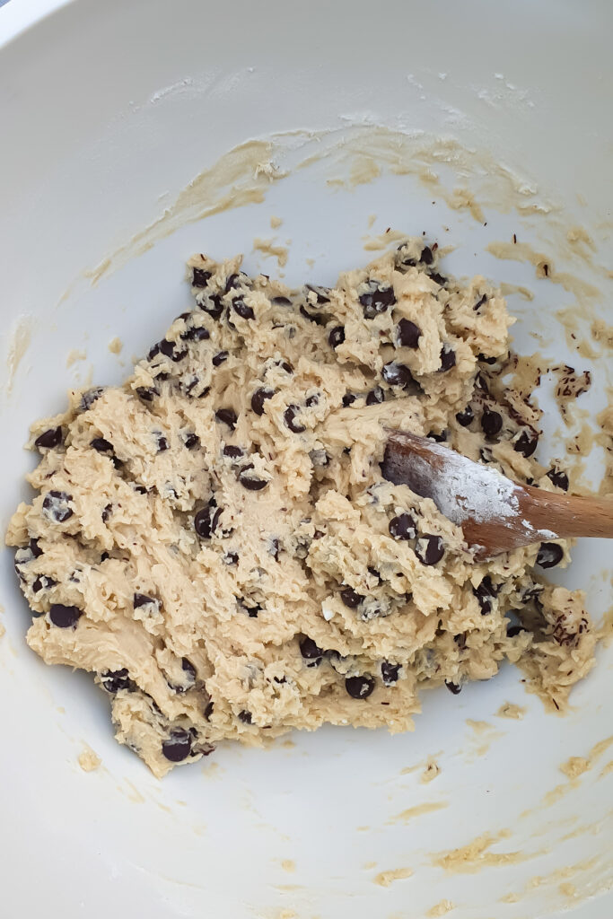 A mixing bowl containing cottage cheese chocolate chip cookie dough being stirred with a wooden spoon.