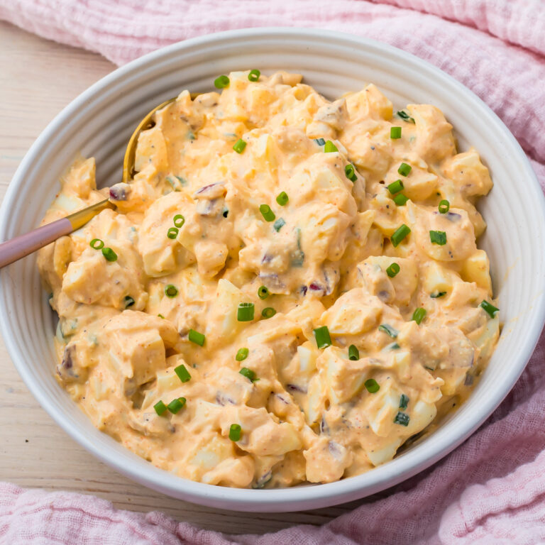 A bowl of creamy egg salad with cottage cheese, garnished with chopped chives, sits ready to enjoy with a spoon resting inside.