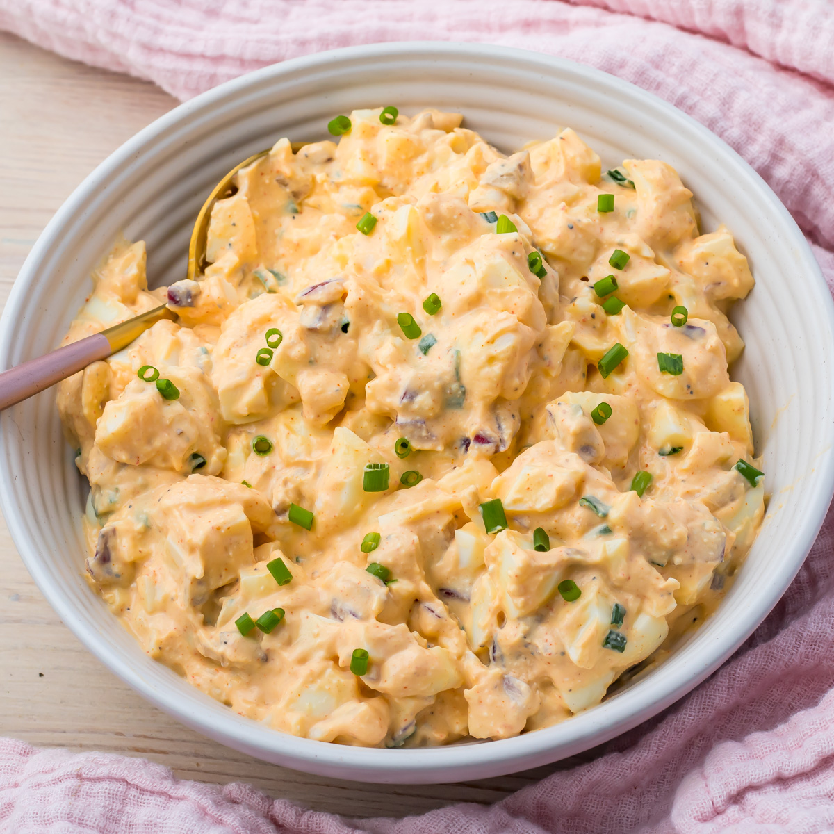 A bowl of creamy egg salad with cottage cheese, garnished with chopped chives, sits ready to enjoy with a spoon resting inside.