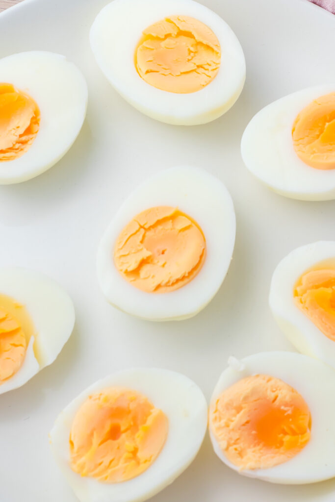 Several hard-boiled eggs cut in half are arranged on a white plate, showing firm, pale yellow yolks and smooth whites—perfect ingredients for a classic egg salad recipe or pairing with creamy cottage cheese.