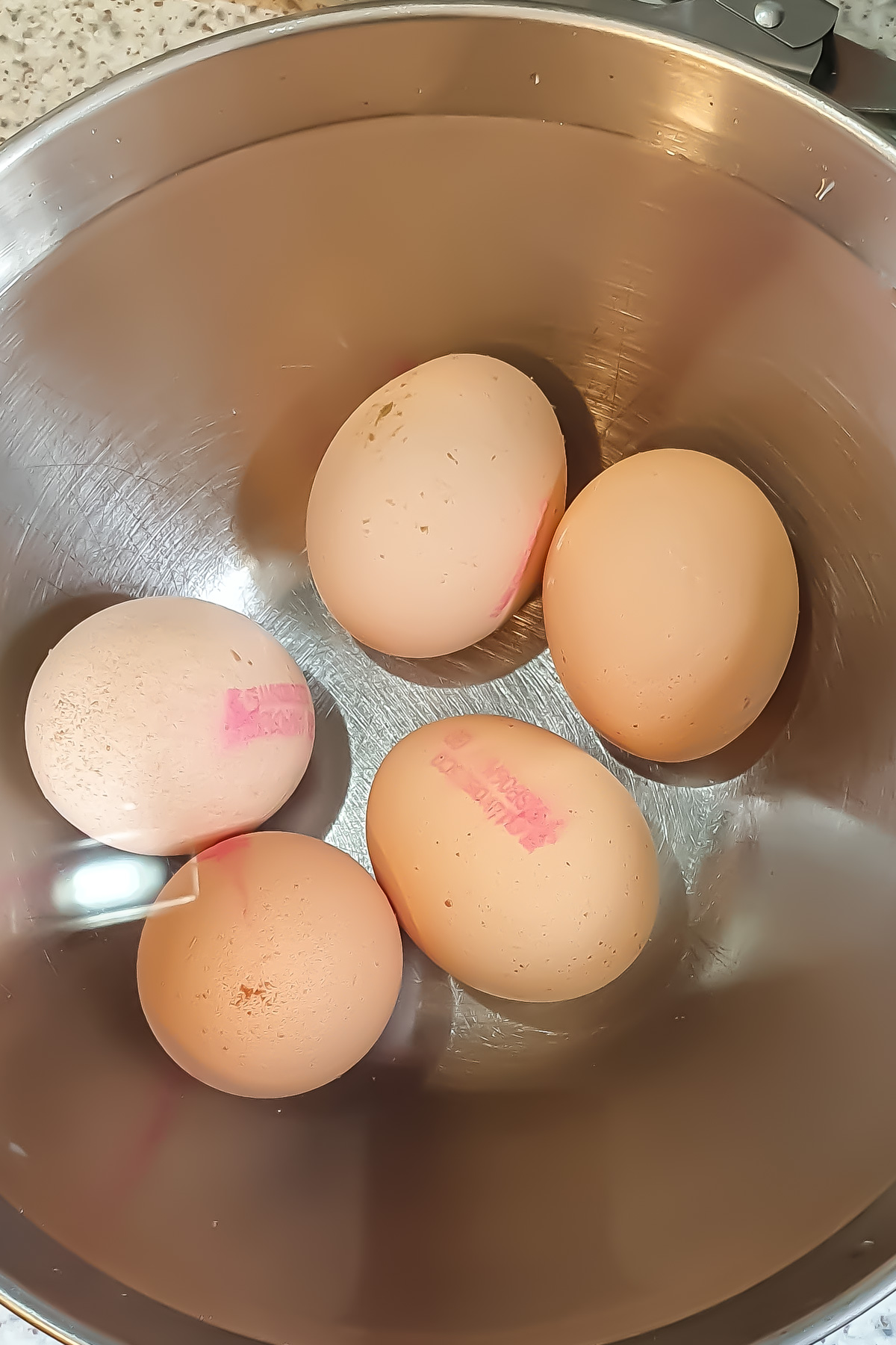 Five brown eggs with pink stamps are placed in a stainless steel mixing bowl, ready to be transformed into a delicious egg salad recipe.