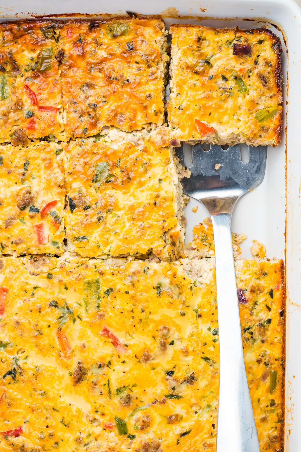 A baked cottage cheese egg bake cut into squares in a white dish, with a metal spatula removing one piece.