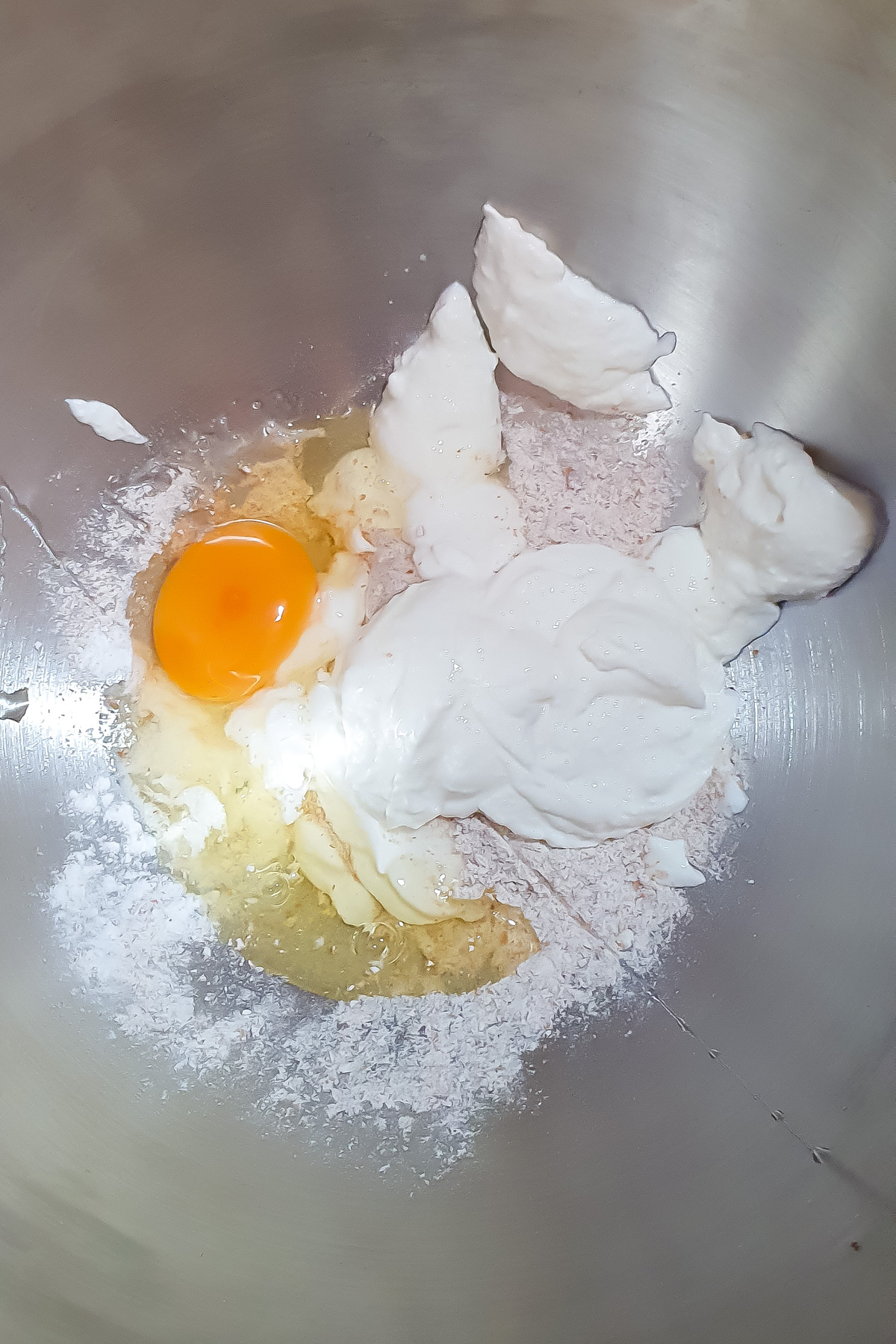 A mixing bowl containing an egg, flour, cottage cheese, and other baking ingredients before mixing.