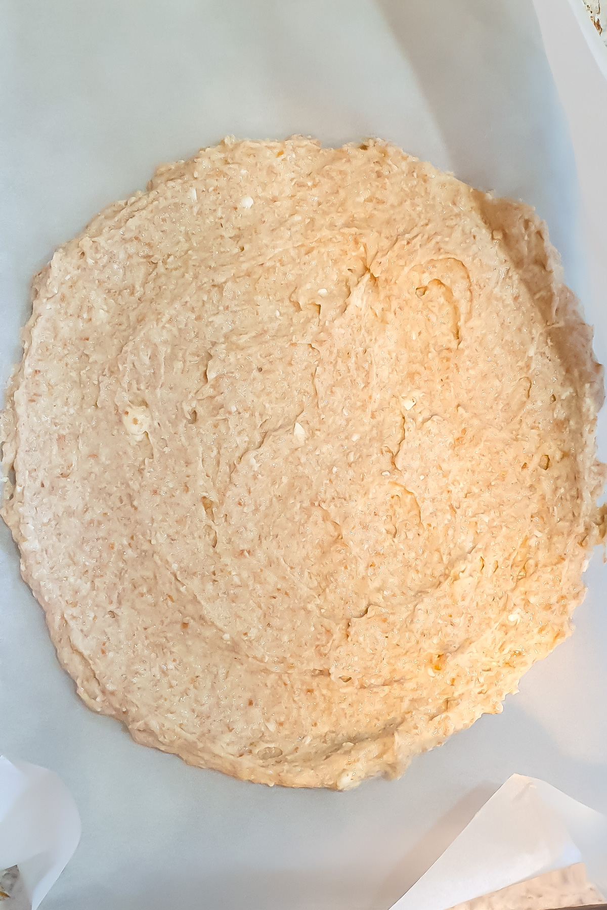 A round, flat layer of uncooked pizza dough or batter spread on parchment paper.