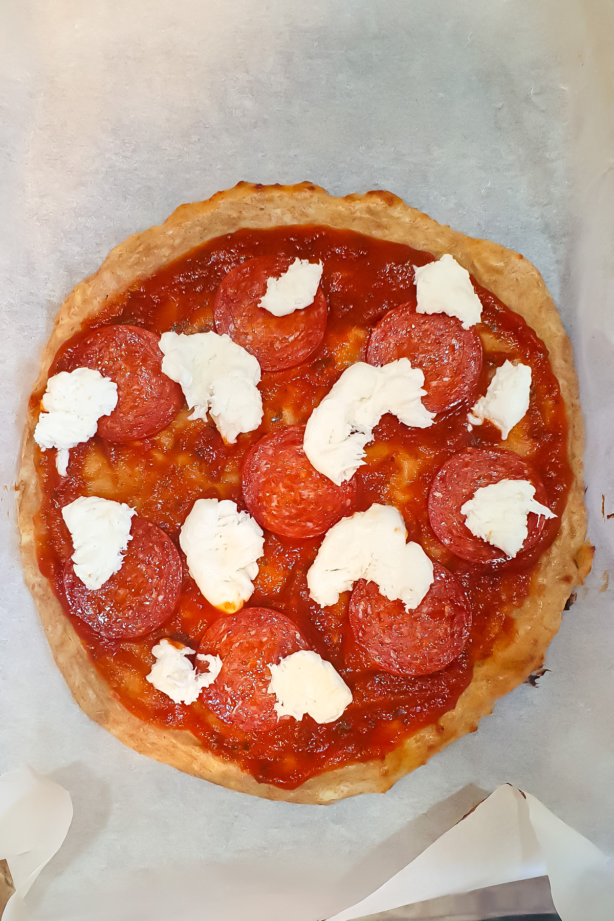 A round Cottage Cheese Pizza with tomato sauce, pepperoni slices, and dollops of white cheese sits on a sheet of parchment paper.