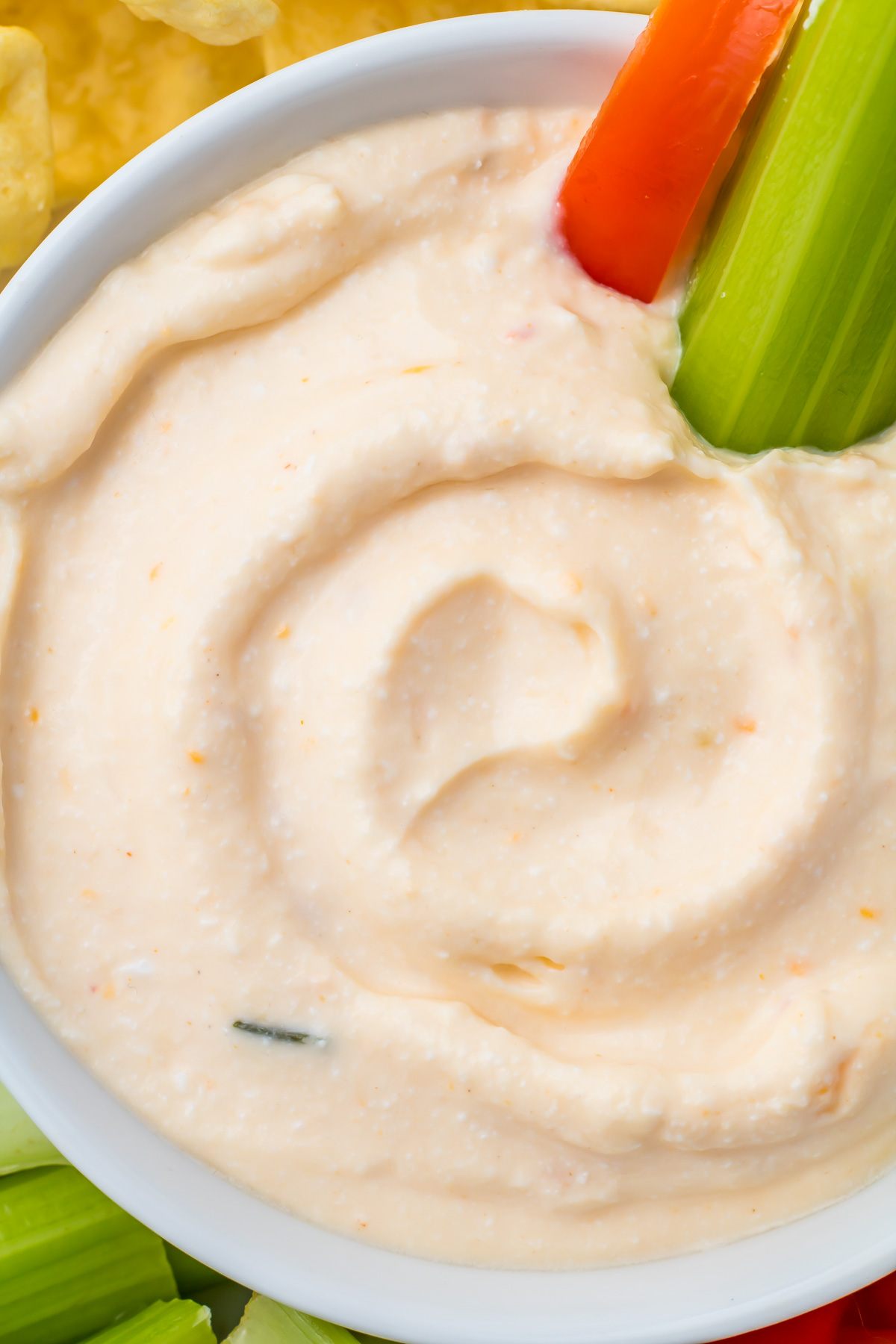 A close-up of creamy Cottage Cheese Queso dip in a white bowl with celery and a red bell pepper slice partially submerged.