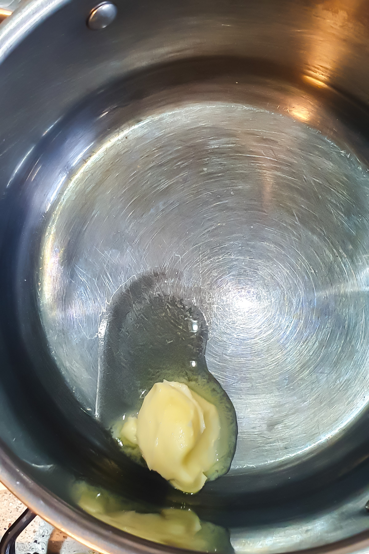 A dollop of butter melting in a stainless steel saucepan on a stove.