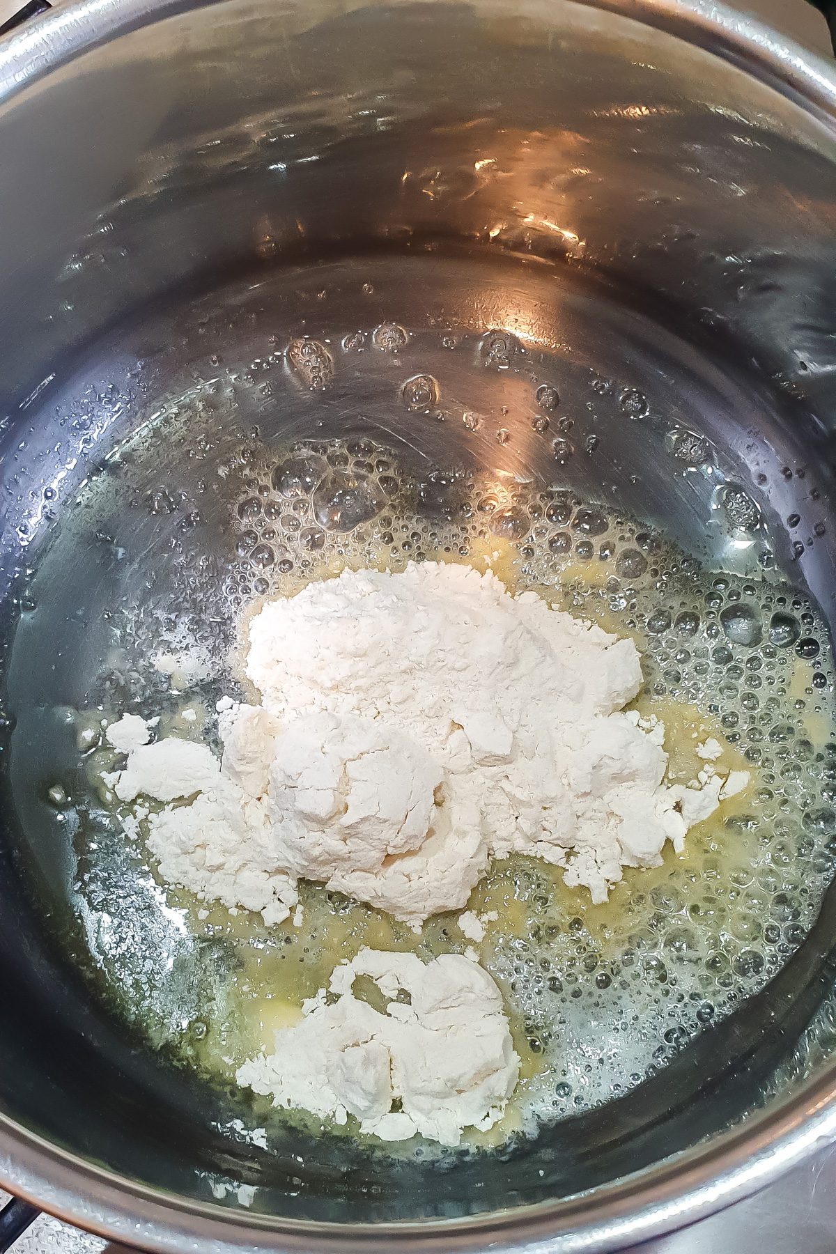 Flour and melted butter are combined in a stainless steel pot, starting the process of making a roux for a creamy cheese dip.